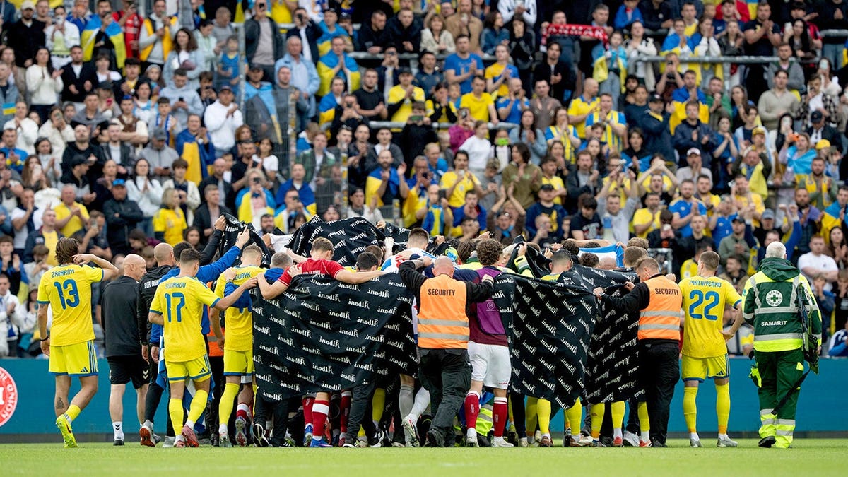 Christian Eriksen being accompanied by Denmark and Ukraine players to an ambulance at Odense Stadium