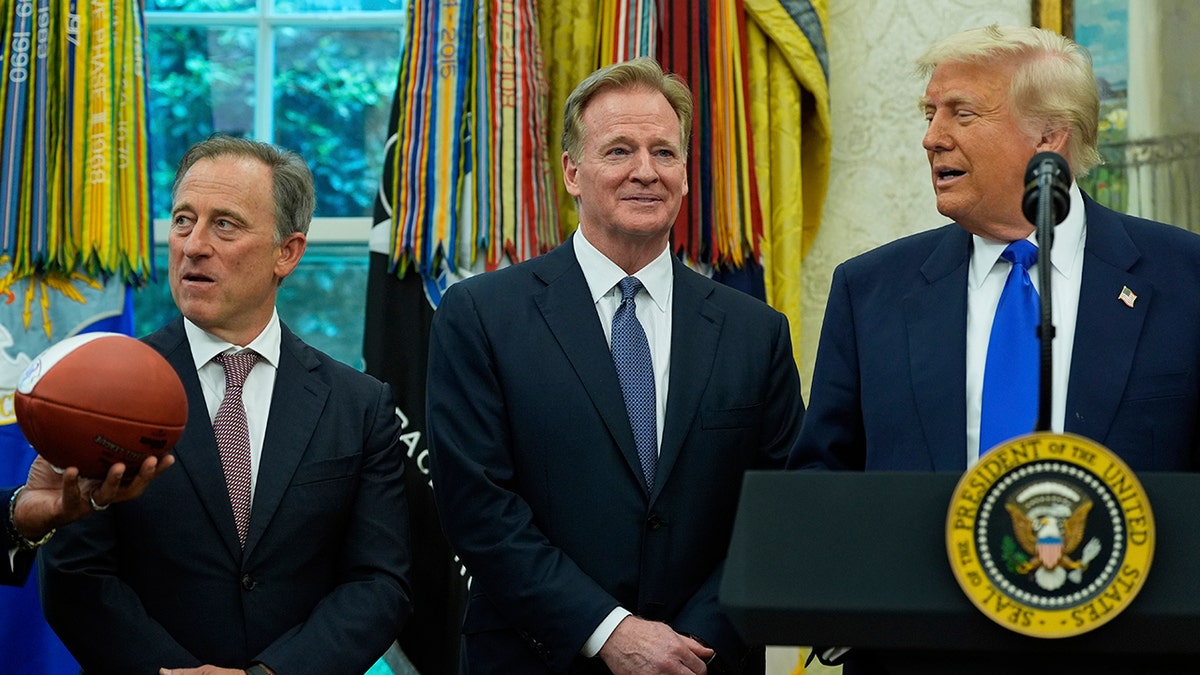 Washington Commanders owner Josh Harris and NFL Commissioner Roger Goodell watch football presented to President Donald Trump in Oval Office