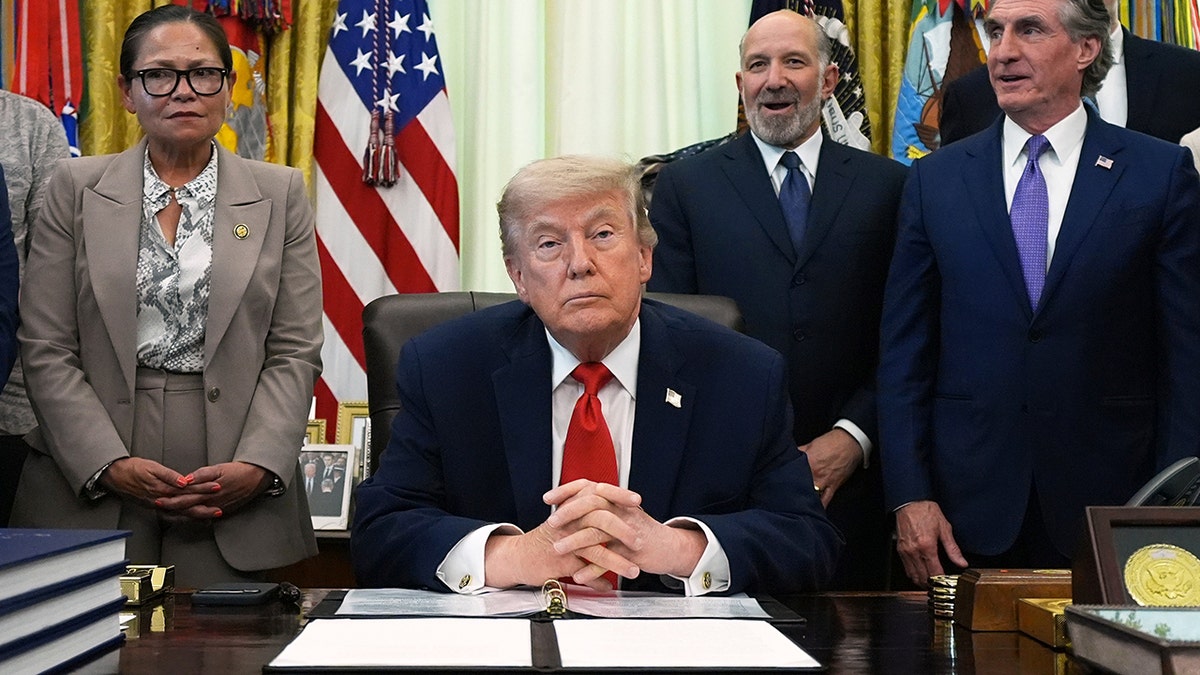 President Donald Trump sitting during an event in the Oval Office with Del. Kimberlyn King-Hinds, Commerce Secretary Howard Lutnick, and Interior Secretary Doug Burgum listening