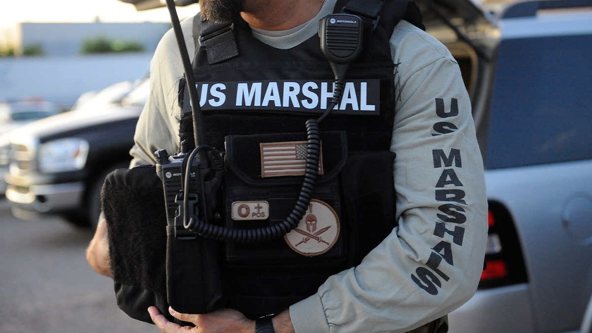 Close-up file photo of a deputy U.S. marshal wearing body armor and tactical gear with a U.S. Marshals Service insignia.
