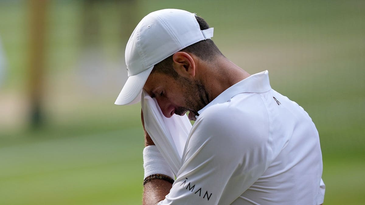 Novak Djokovic wipes away sweat during a tennis match.