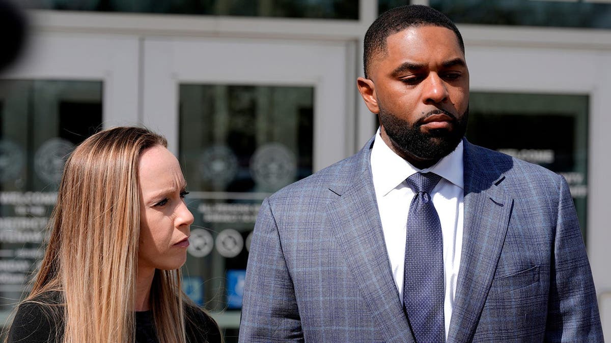Sherrone Moore and his wife Kelli Moore listen to lawyer Ellen Michaels speak in a courtroom.