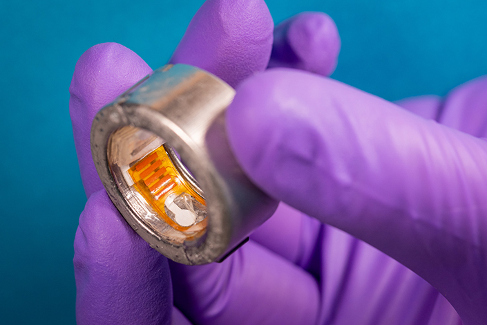 A purple-gloved hand holding a smart ring.
