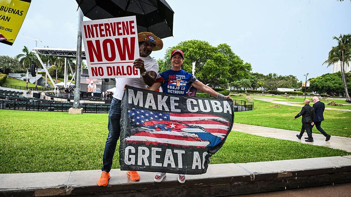 People hold a placard and banner in the rain at a Free Cuba rally in Miami.
