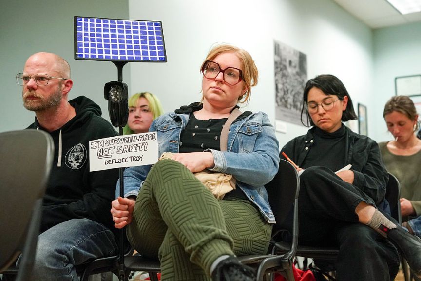 A person protesting Flock at a city council meeting.