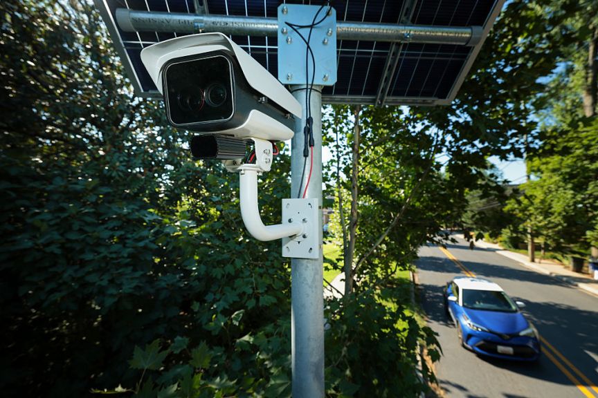 An ALPR camera next to shrubs.