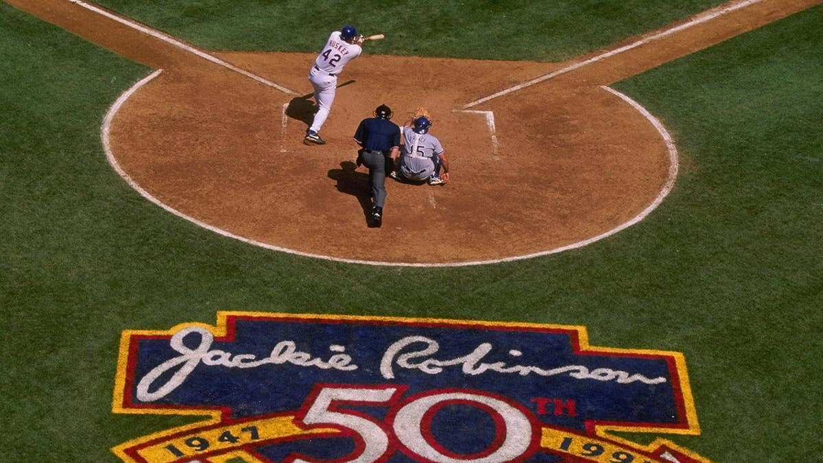 Butch Huskey of the New York Mets stands at bat behind home plate with Jackie Robinson memorial art visible on the field.