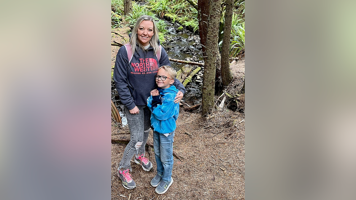 Jessica Orton Lyman poses with her son Eli Painter beside a wooded stream