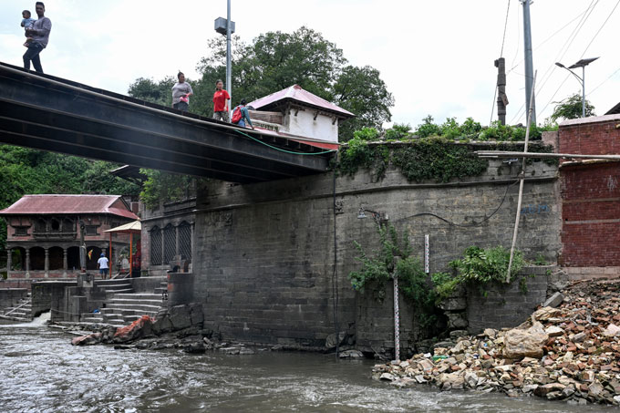 Several people walk over a bridge in Kathmandu that has a siren designed to provide flood warnings.