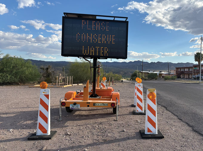 A portable electronic road sign in Kearny, Arizona, displays the message “Water shortage warning” against a mountainous desert landscape.