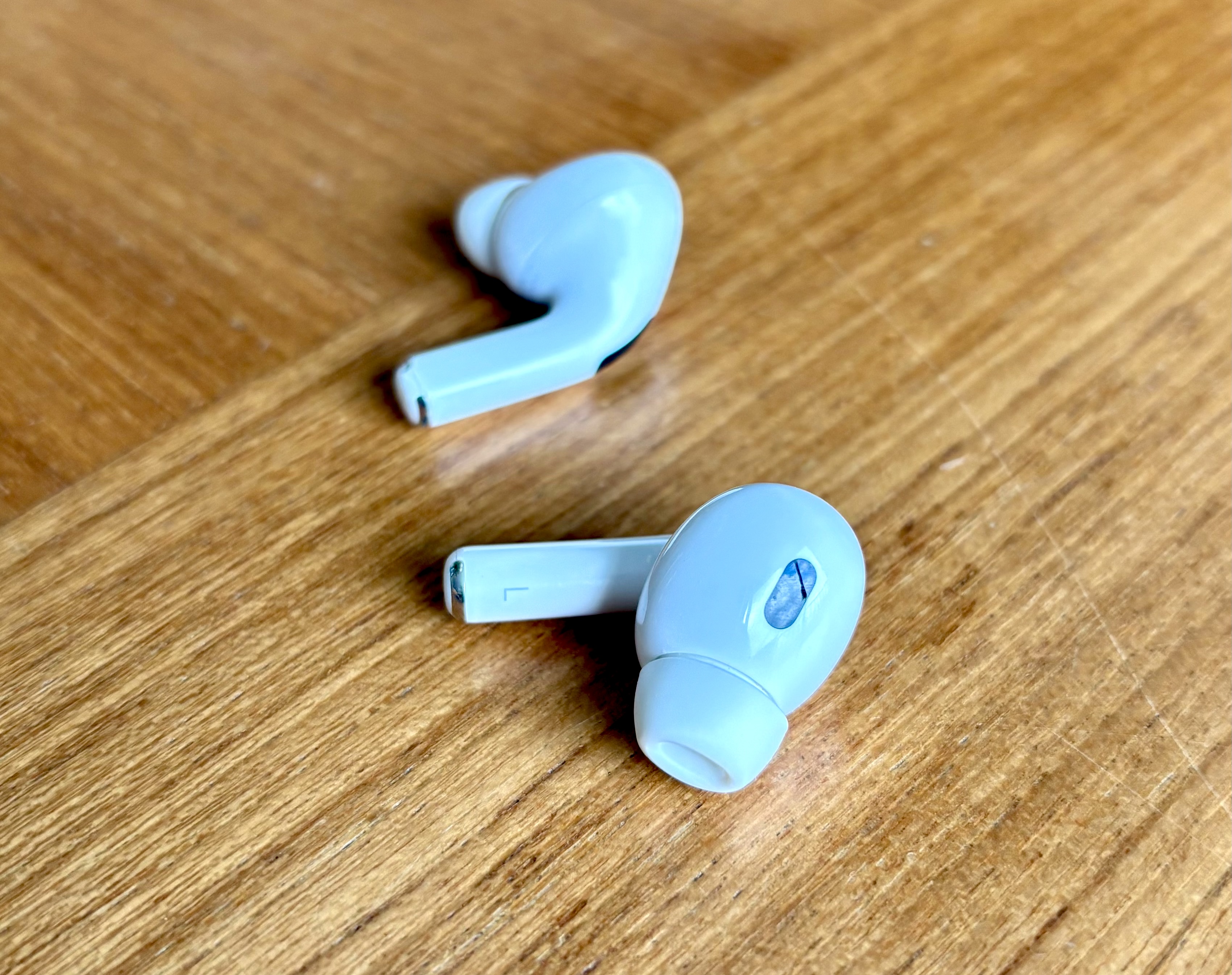 Two AirPods Pro 2 earbuds on a warm wood surface.