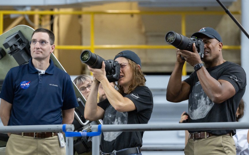 A man and a woman holding DSLR cameras with long lenses train how to use them.