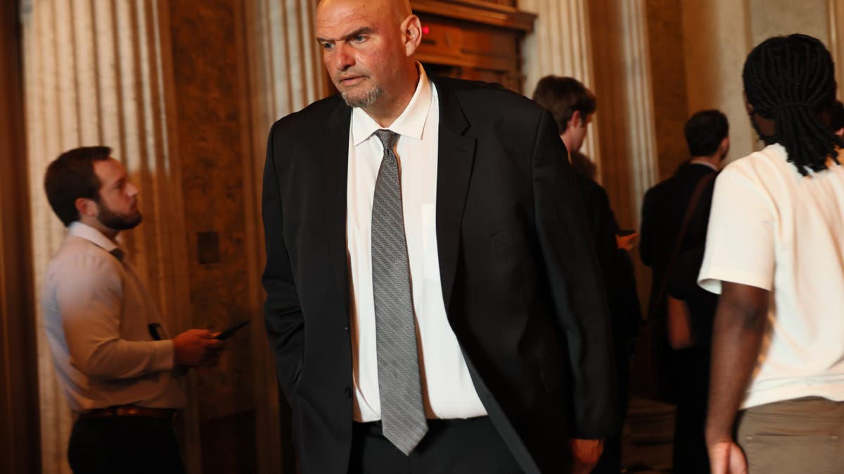 john fetterman pictured in a black suit and tie in a government building