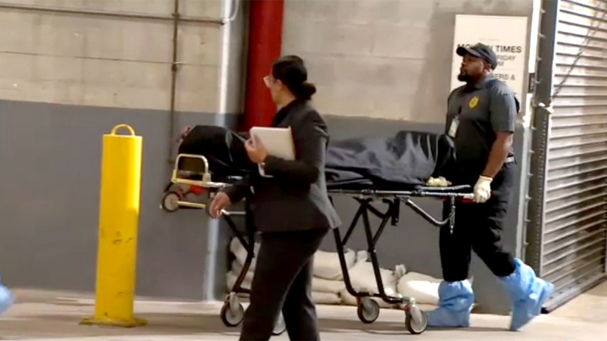 officials remove a body in a black body bag from the scene