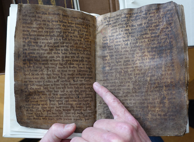 A finger points to writing in an old book. The text is a poem that alludes to the impact of a volcanic eruption on the atmosphere over Iceland.