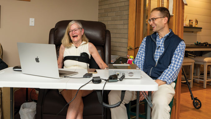 A woman hooked up to a computer smiles as she sits next to a male scientist.