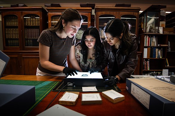 University of Sydney students Jasmine Digges, Neha Jyoti, and Nidhi Dabadghav look at glass plate photo negatives taken by Michael Sharland.