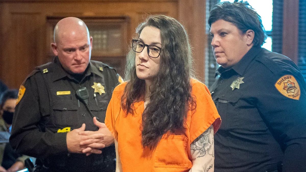 Bailey Boswell being escorted by police in court while wearing an orange jumpsuit.