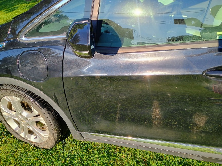 A black driver-side door after being washed with a power washer. A few mud splotches are still visible, and the tire is still fairly muddy.