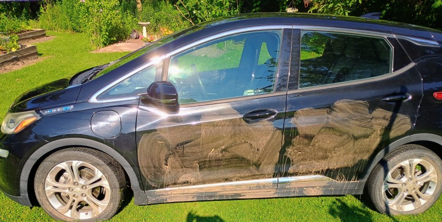 A black sedan with mud smeared on the driver-side tires and doors.