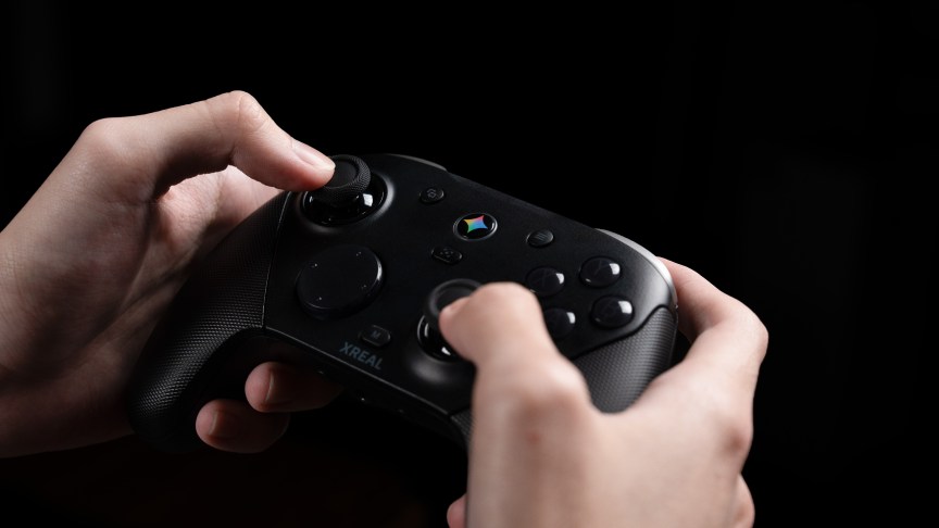 Two hands hold a black game controller that has a Gemini button in the center.