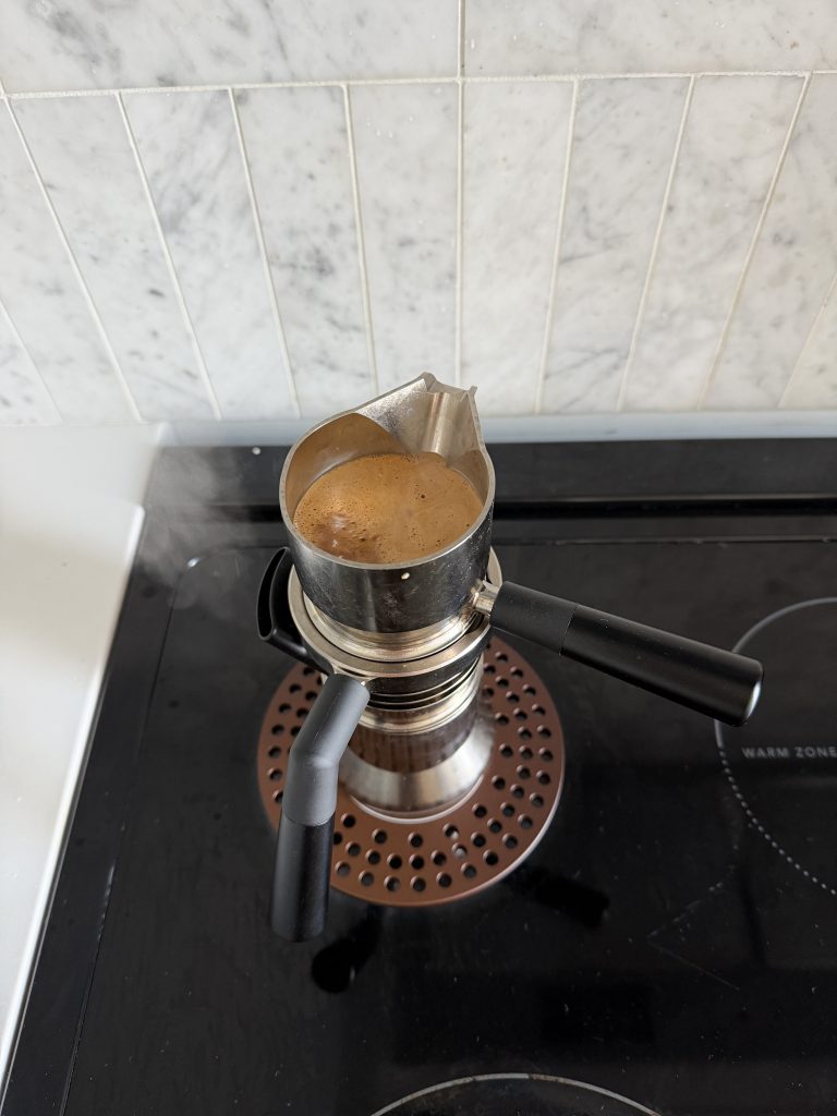 Steam comes out of the side of the 9Barista espresso maker as espresso fills the funnel at the top.