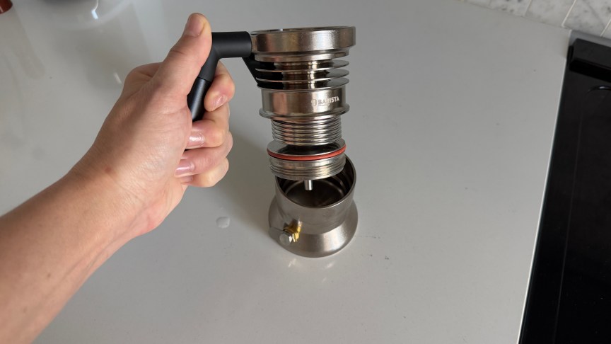 A person's hand holds a 9Barista espresso maker partially disassembled to show how the three parts come together.