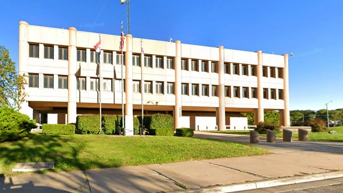 Exterior of a three-story Independence Police Department building with flags flying in front, a grassy lawn and a clear blue sky.