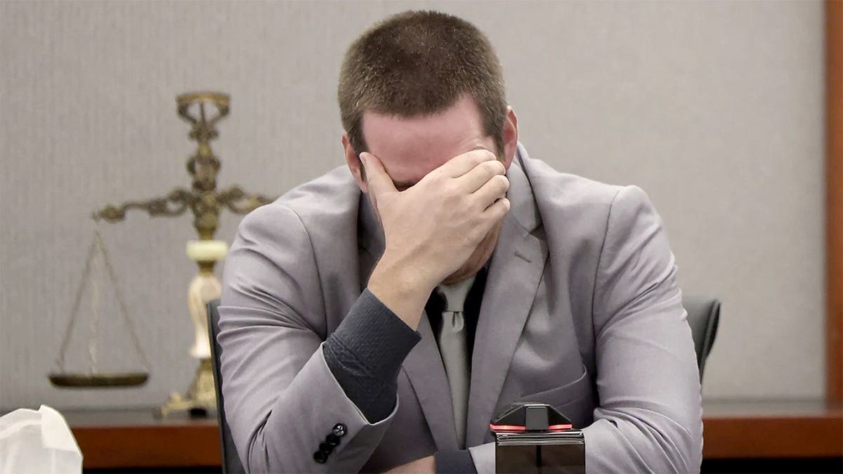 Mitchell Fairbarn sits in a Las Vegas courtroom wearing a gray suit, leaning forward with one hand covering his face.