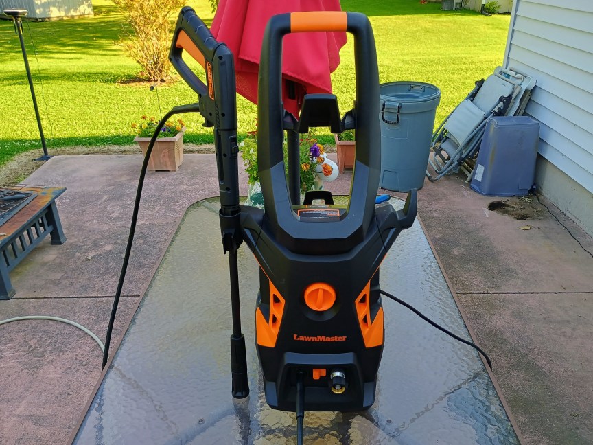 A black and orange LawnMaster LT506-2000A power washer sits fully assembled on a glass tabletop on a patio.