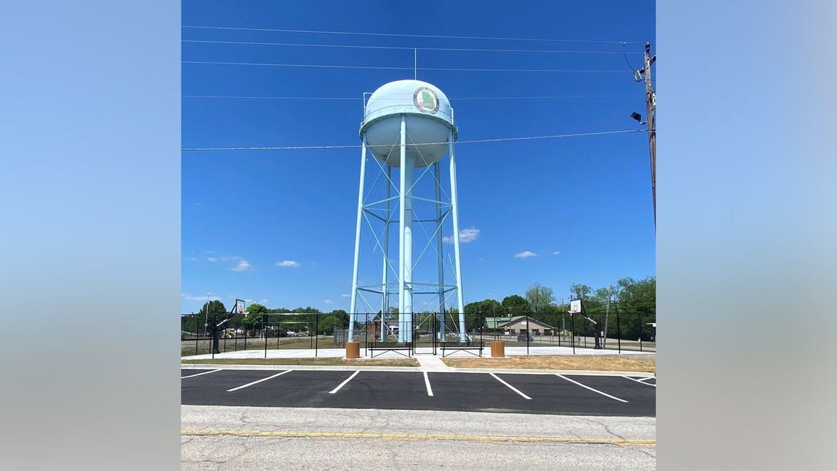 A light blue water tower rises above basketball courts and a parking lot in Milner, Georgia.