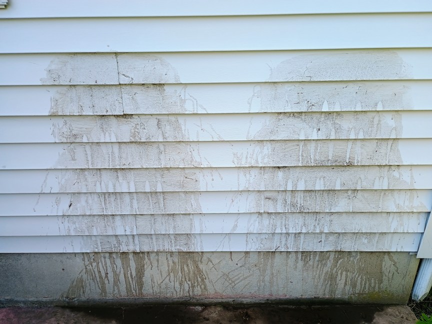 Two areas of light-colored house siding are covered in a mud slurry before being used to test power washers.
