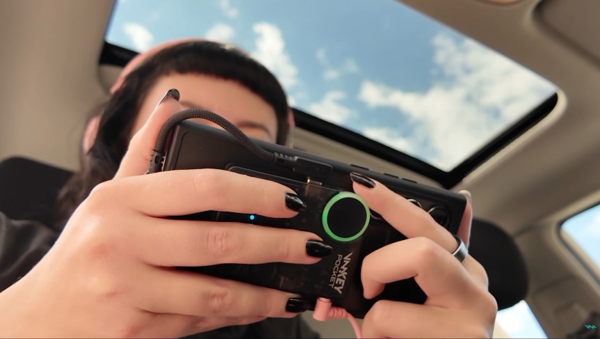 A person holds their phone in front of them with a device on the back, using their fingers to press the buttons and wheel on the device.