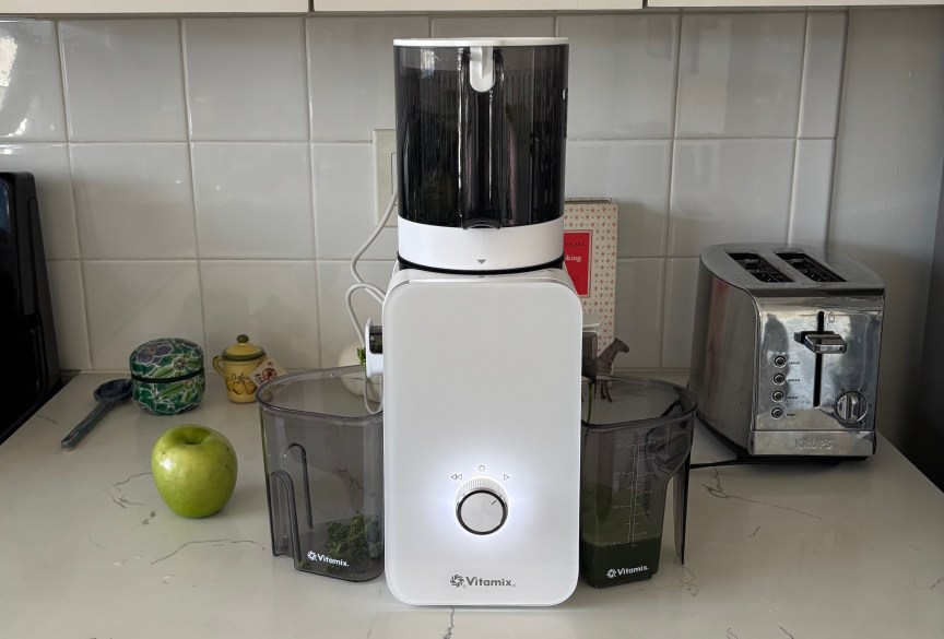 The white Vitamix MaxExtract juicer on a white countertop next to a green apple.
