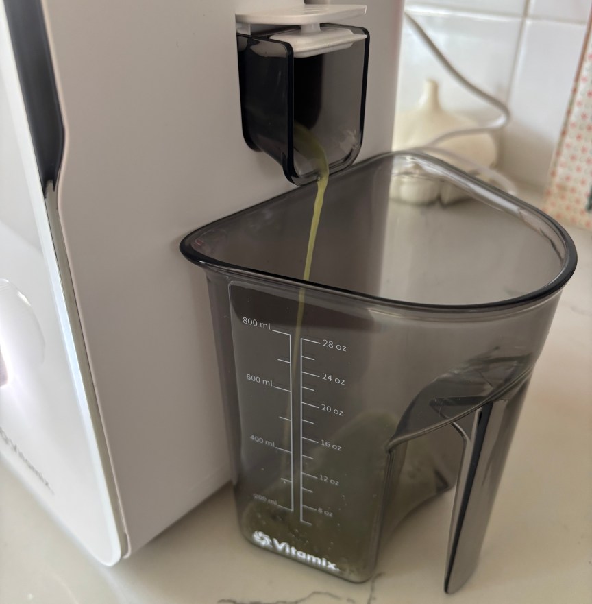 The Vitamix MaxExtract pouring green juicer into a gray container with measurements.