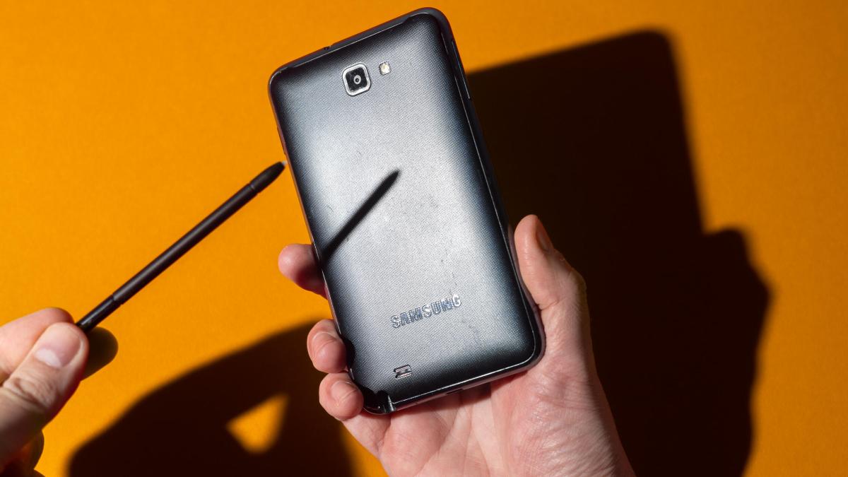 A hand holding a Samsung Galaxy Note while the other holds a stylus over its screen