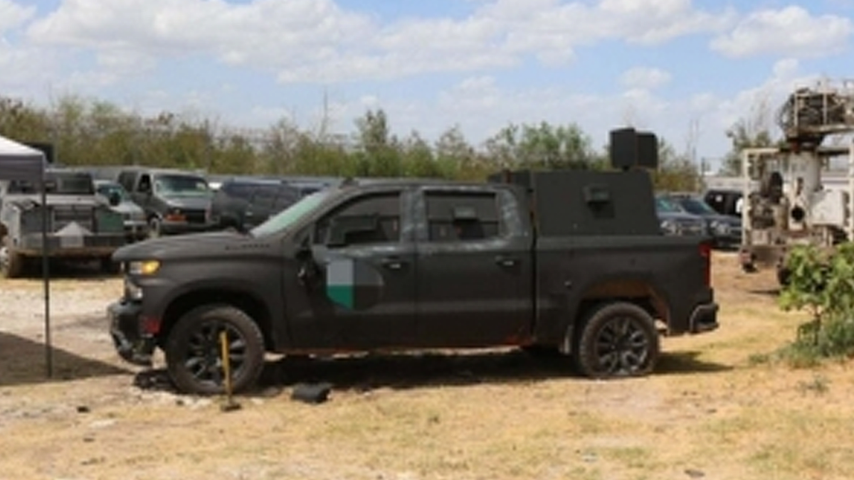 An armored black pickup truck is parked in a lot with other vehicles