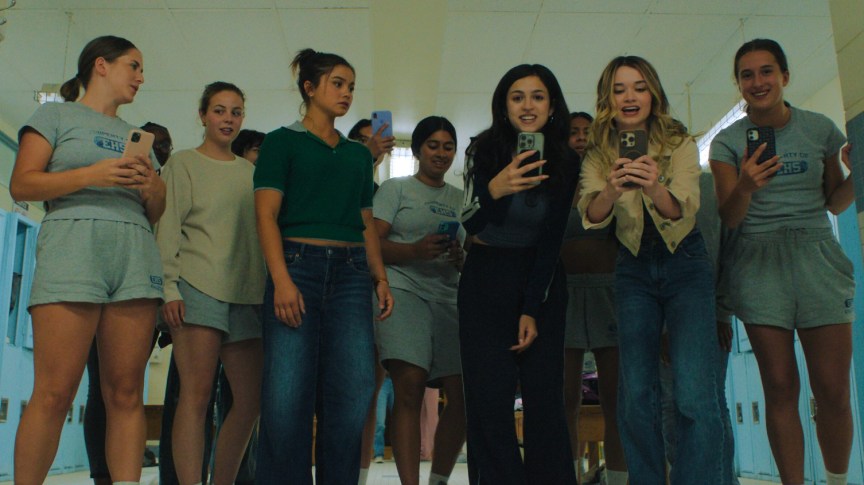 A group of girls record on their smart phones in a high school locker room.