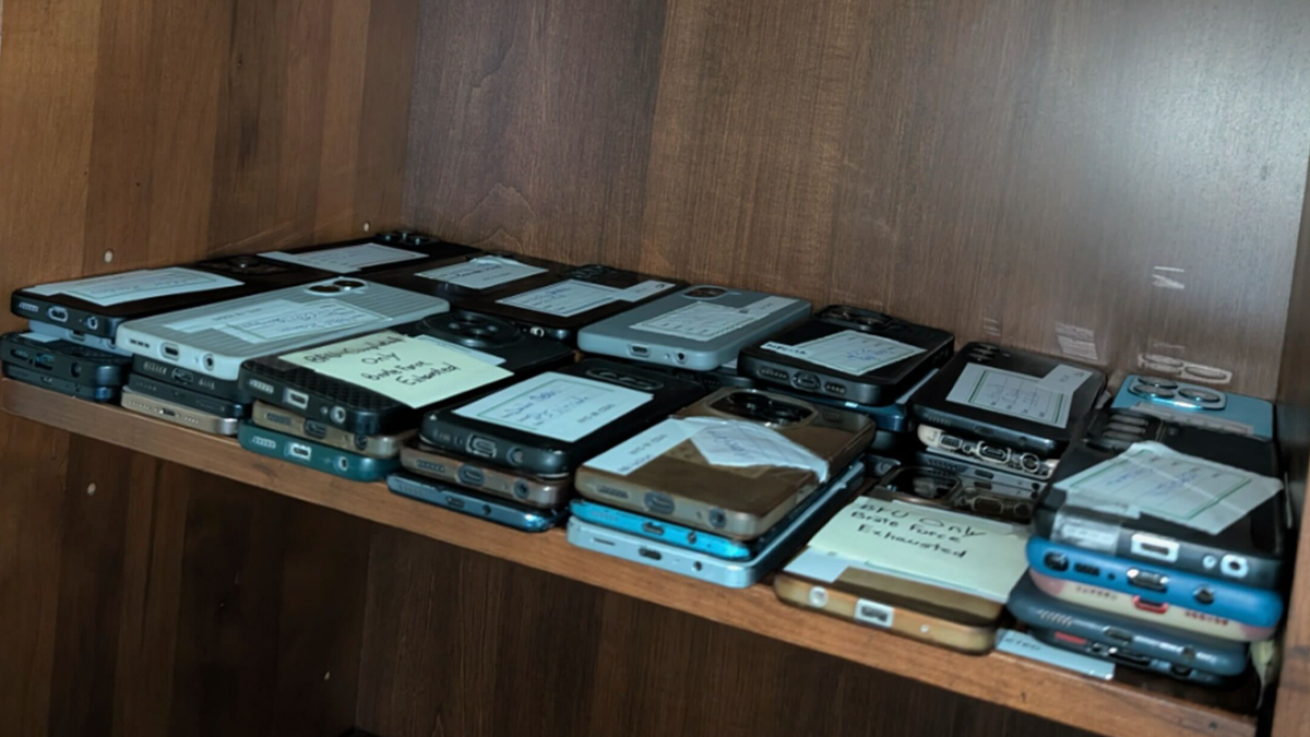 Dozens of labeled smartphones arranged on a wooden shelf during a scam center investigation in Ghana