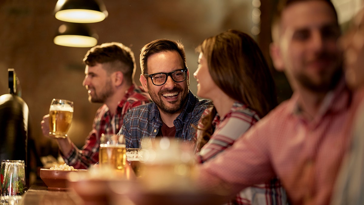 A man talks to a woman while they drink beers at a bar.