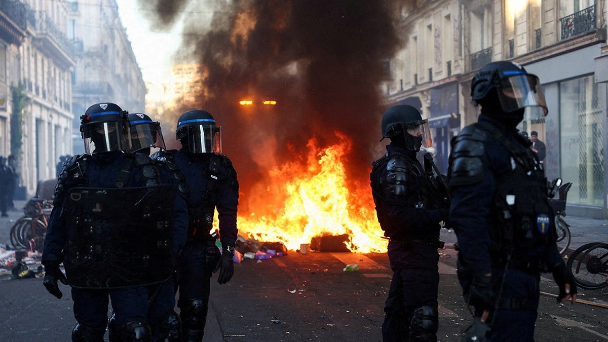 Police officers in riot gear stand guard near a fire during civil unrest in Paris.