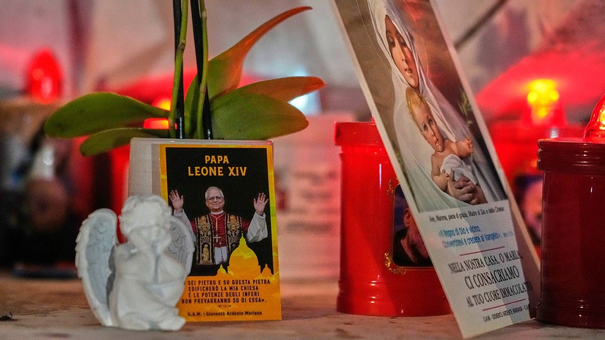 Pope Leo XIV image rests at the base of a statue of Pope John Paul II outside a hospital in Rome.