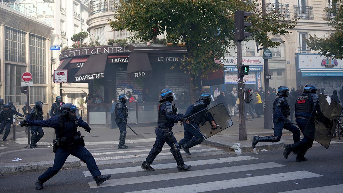 Riot police officers run across a street during protests in Paris.