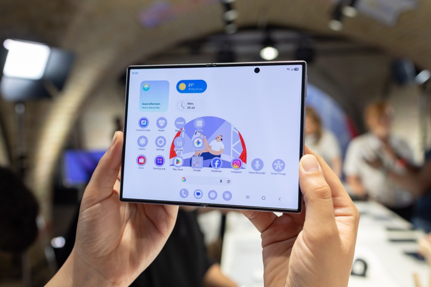 A foldable phone being held up in front of a busy room.
