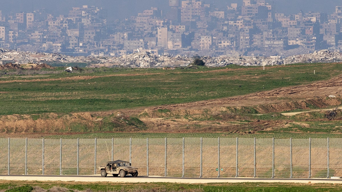 A military vehicle drives along a fenced border area overlooking open terrain.